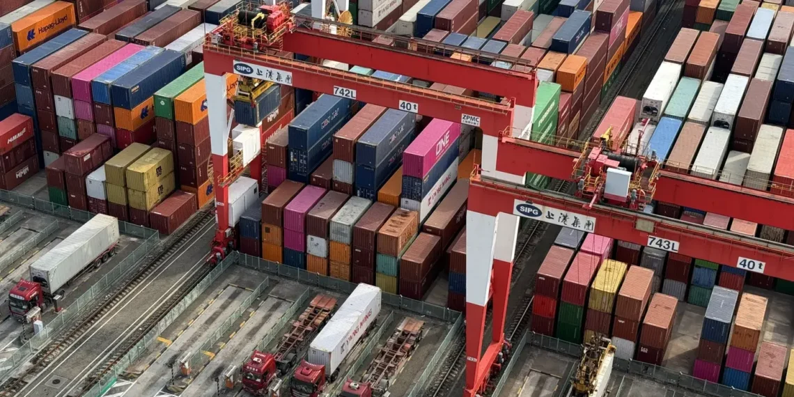 Aerial view of stacked shipping containers and cargo cranes at a busy port terminal, representing global trade and international shipping logistics.