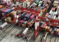 Aerial view of stacked shipping containers and cargo cranes at a busy port terminal, representing global trade and international shipping logistics.