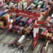 Aerial view of stacked shipping containers and cargo cranes at a busy port terminal, representing global trade and international shipping logistics.